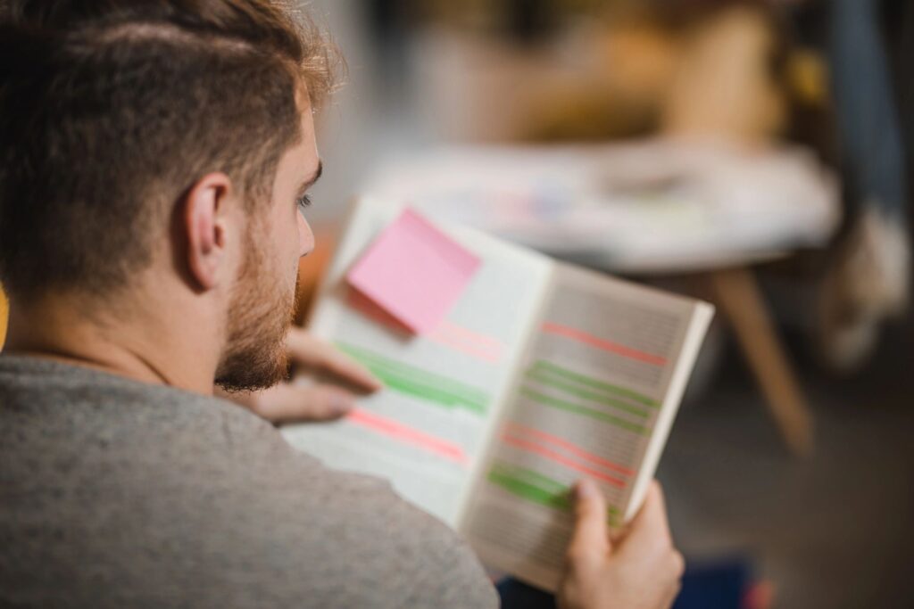 Close up of male student reading book while learning at campus.